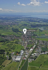 Luftbild eines kleinen Dorfes mit grünen Feldern und Landwirtschaft nahe einem See, ideal für nachhaltigen Hausbau.