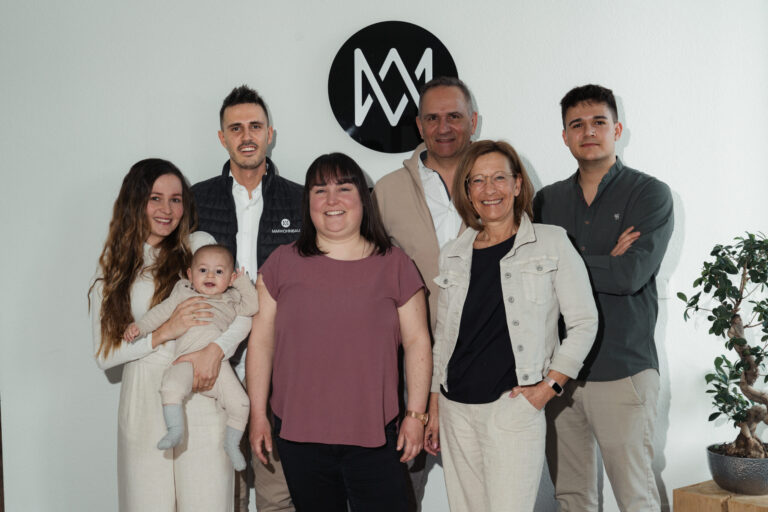 70 – DSC03153 Gruppenfoto eines Bauunternehmens mit einer Familie vor einem weißen Wall; die Frau hält ein Baby und daneben steht eine Pflanze im Topf.