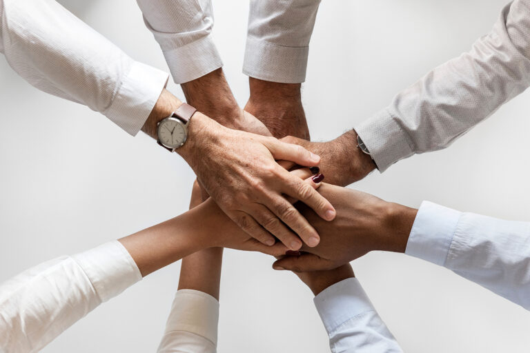 rawpixel-558597-unsplash.jpg Gruppe von Menschen hält Hände ineinander, symbolisiert Teamwork und Zusammenarbeit im Massivhaus-Bau.